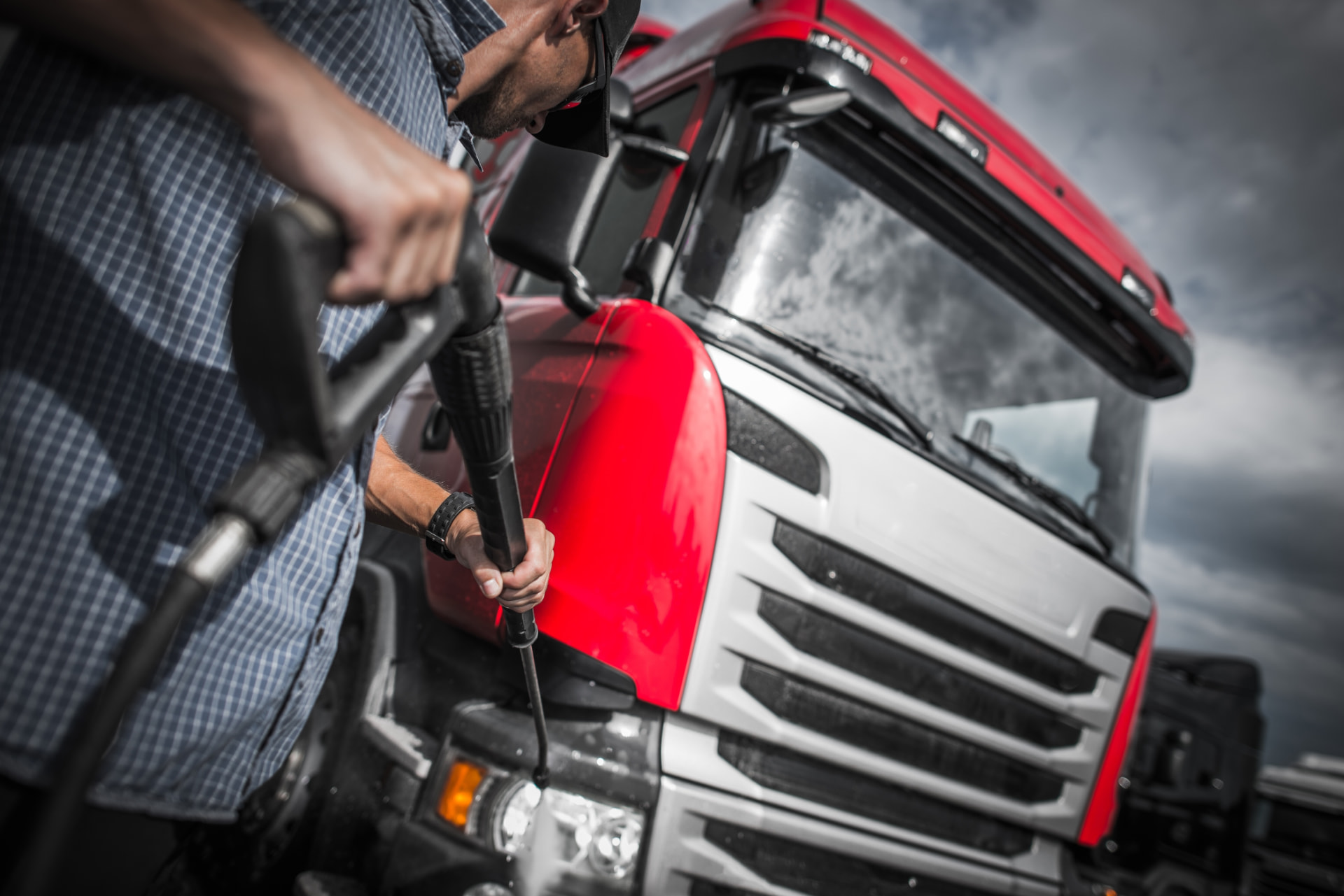A driver pressure-washing the hood of a red semi-truck