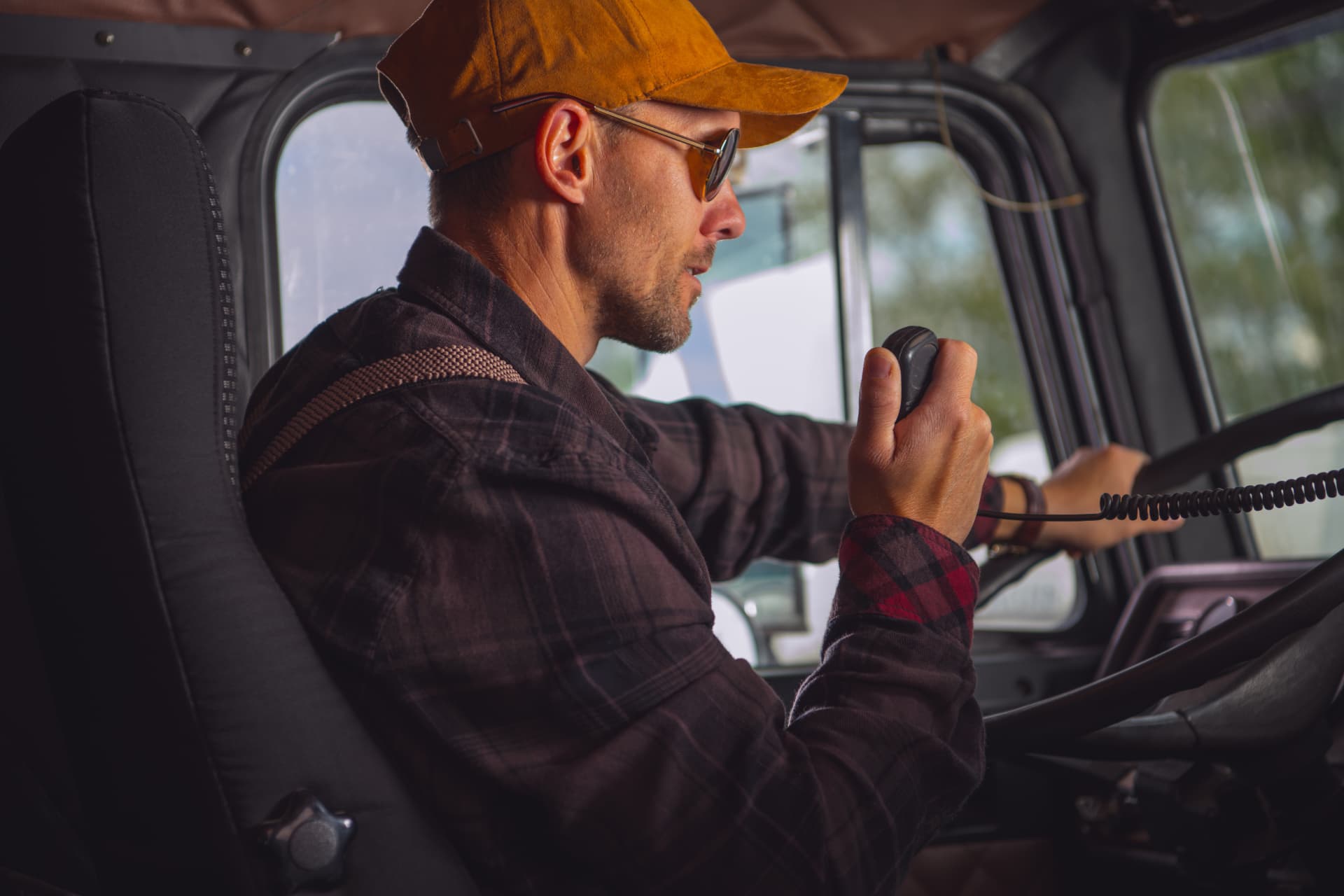 A truck driver in the cab of a semi speaking into a radio handset