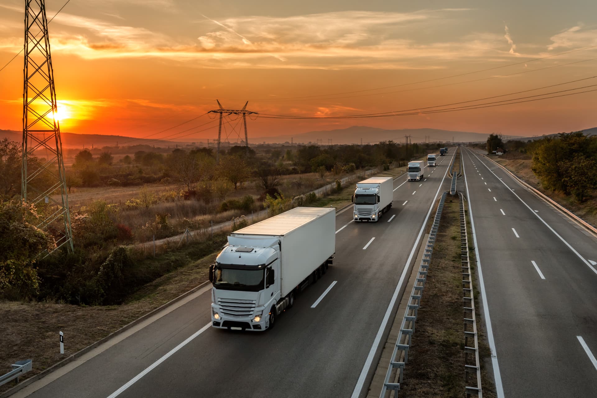 A convoy of tractor-trailers running an interstate lane at sunset