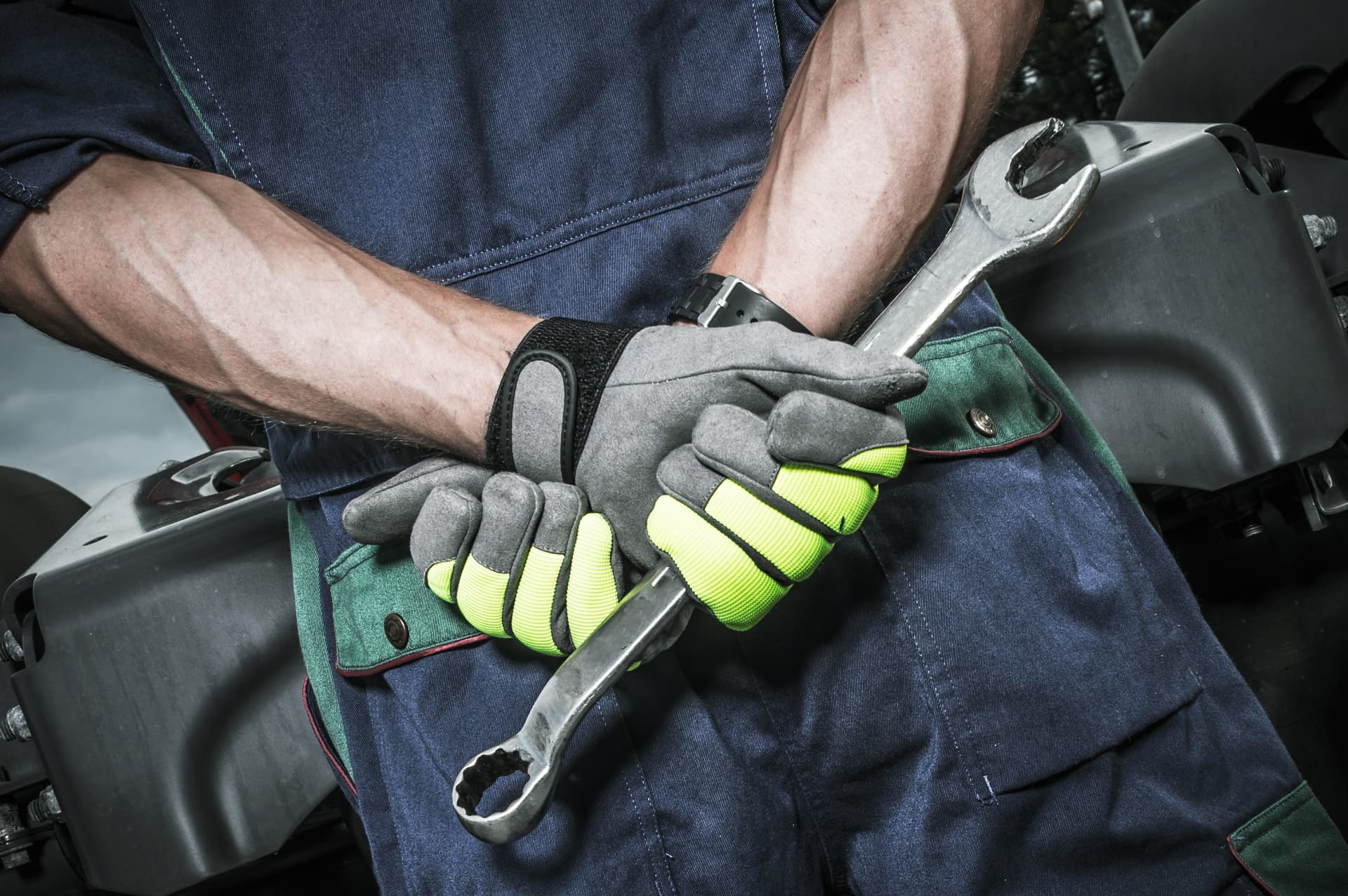 A diesel mechanic in coveralls holding wrenches beside an opened engine